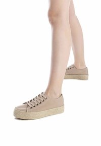 Zapatillas de lona beige con punta redonda, diseño de cordones y suela de cuña envuelta en yute. Textura suave con un detalle mínimo.