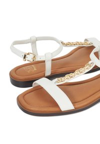 Witte platte sandalen met een beige zool, met twee brede banden en een gouden kettingaccent. Verstelbare enkelriem met een metalen gesp.