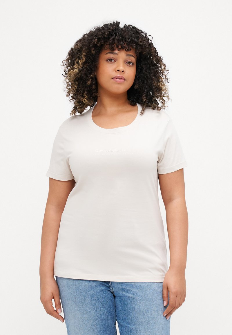 Tricou scurt cu mânecă, de culoare bej deschis, cu un gât rotund, fabricat dintr-un material moale, având un logo subtil imprimat pe piept.