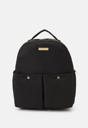 Sac à dos en nylon noir de forme arrondie, avec des accents dorés, deux poches avant et une poignée supérieure. Il comporte une fermeture zippée et une plaque avec le logo.