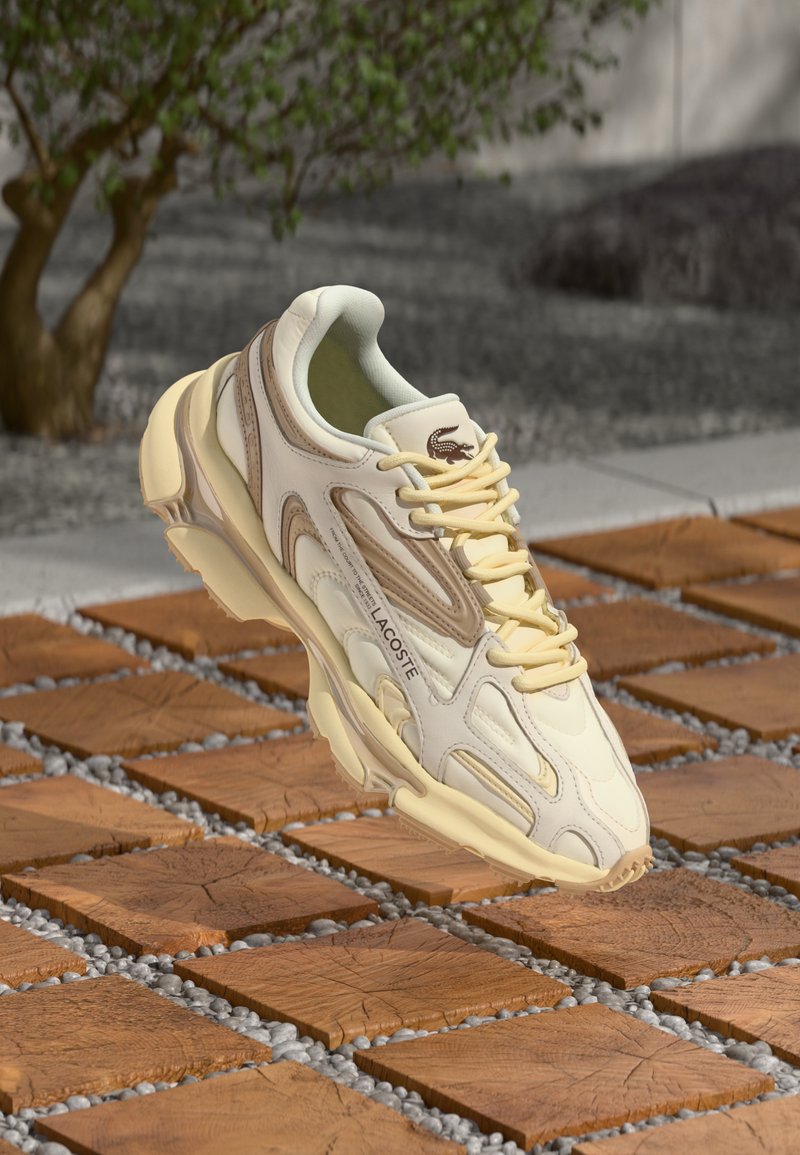 Baskets Lacoste en crème et jaune clair avec une tige texturée, une semelle épaisse et un branding subtil. Conçues dans un style sportif avec un laçage à l'avant.