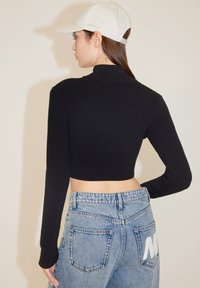Suéter negro acanalado cortado con mangas largas, combinado con jeans de tiro alto de color azul claro que presentan un logo blanco en el bolsillo trasero.