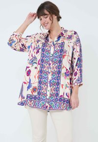 Floral patterned blouse in cream, featuring colorful accents, buttons, and three-quarter sleeves. The fabric has a smooth, lightweight texture.