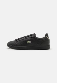 Baskets en cuir noir avec une surface texturée, dotées d'un bout rond, d'un design à lacets et d'un logo vert brodé sur le côté.