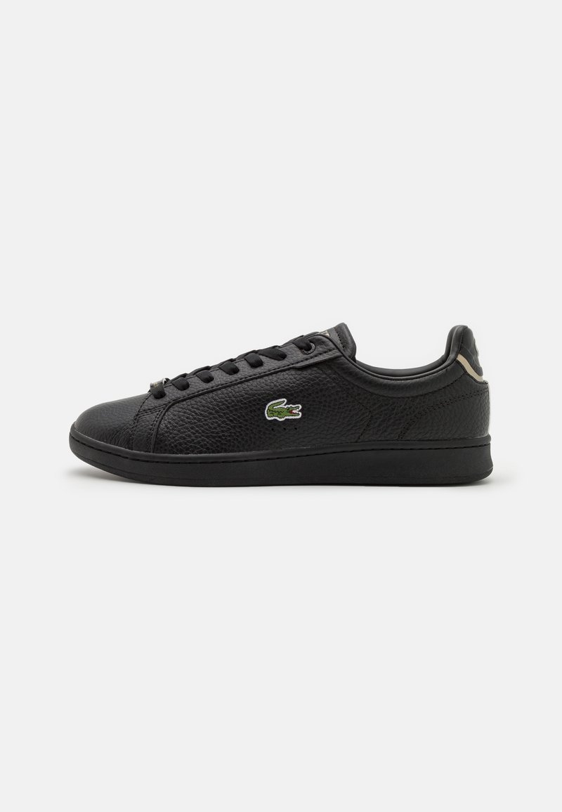Baskets en cuir noir avec une surface texturée, dotées d'un bout rond, d'un design à lacets et d'un logo vert brodé sur le côté.