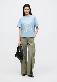 Lyseblå bomulls t-skjorte med hvit tekst, kombinert med olivengrønne vide cargobukser med lommer. Svart håndveske og flate sko.