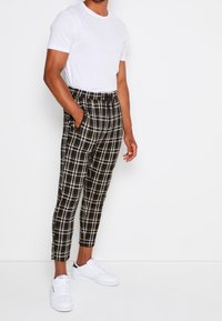 Spodnie w czarno-białą kratę ze ściągaczem w pasie, zestawione z prostym białym t-shirtem i białymi trampkami.