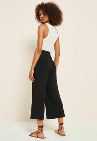 Črne široke hlače iz mehkega materiala z elastičnim pasom. V kombinaciji z belo brezrokavno majico in ravnimi sandali.
