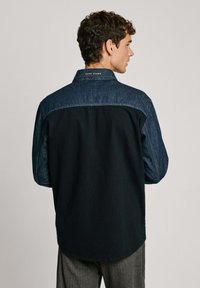 Camicia da uomo con corpo nero, yoke e maniche in denim scuro, colletto button-down e orlo curvo. Logo "Pepe Jeans" sul colletto.
