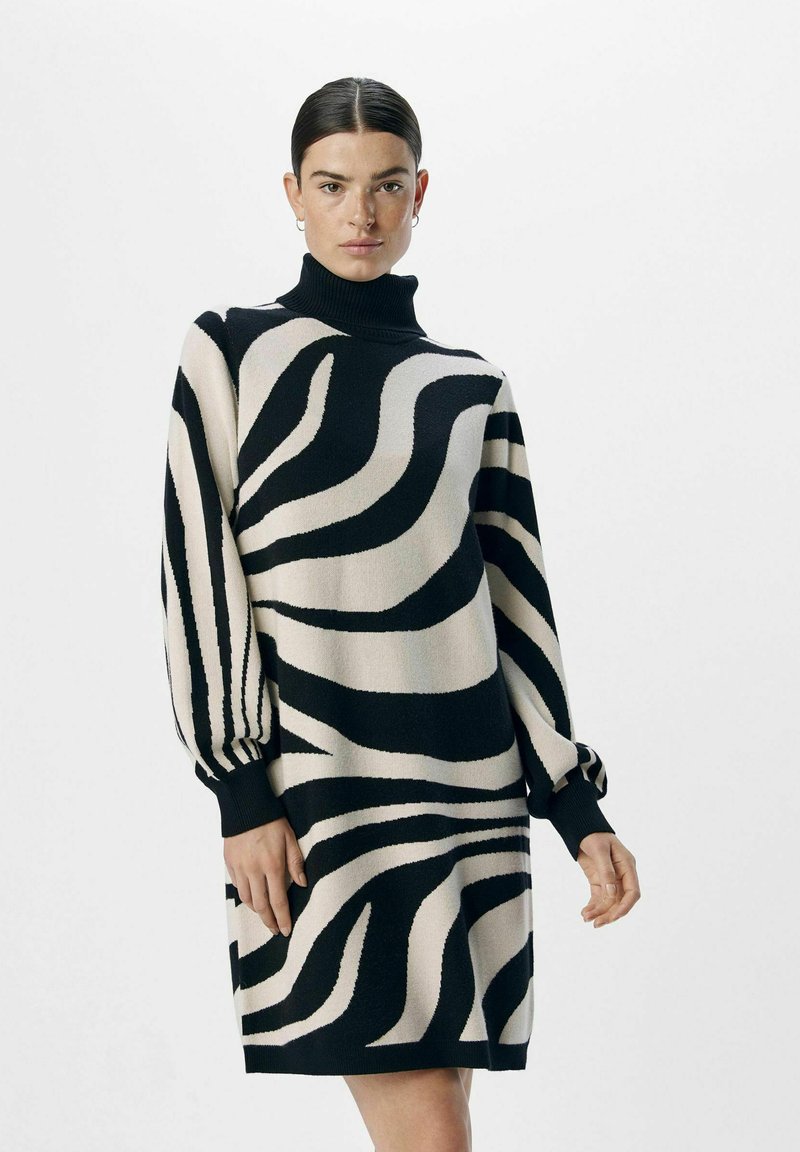 Robe en tricot avec un col roulé haut, des rayures zèbre noires et crème, des manches ballons et des poignets côtelés, offrant une coupe décontractée et une texture douillette.