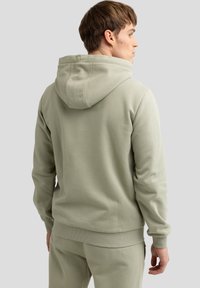 Hellgrüner Hoodie mit Kordelzugkapuze, gerippten Bündchen und einer weichen Textur. Die Rückseite zeigt ein minimalistisches Design ohne sichtbare Logos.