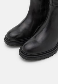 Bottines en cuir noir à finition lisse, bout arrondi, semelle en caoutchouc texturée et détail zippé sur le côté.