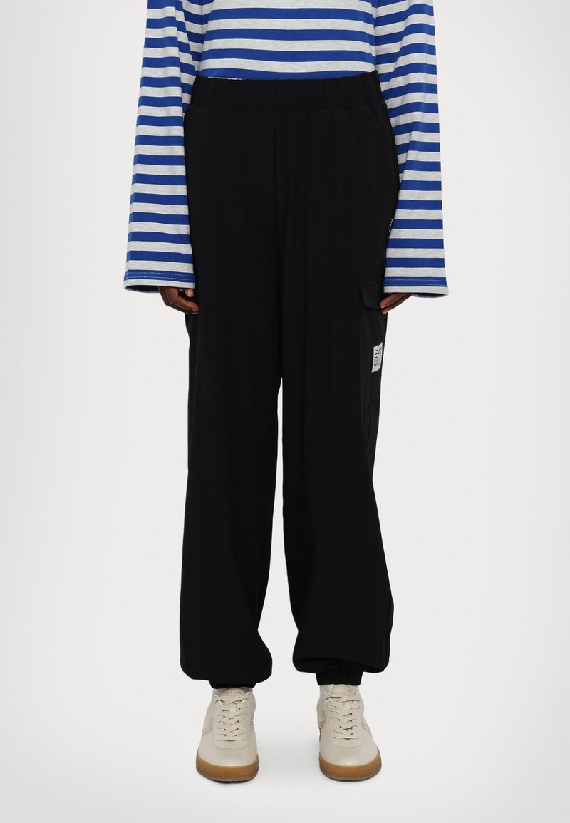 Μαύρο παντελόνι με φαρδιά μπατέτα και ελαστική μέση, με πλαϊνές τσέπες και ένα μικρό λογότυπο. Φοριέται με μπλούζα μακρυμάνικη σε μπλε και γκρι ρίγες.