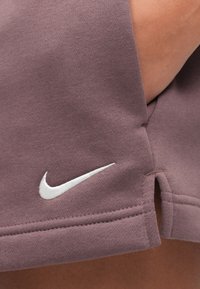 Κοντινή εικόνα βερμούδων από ύφασμα μωβ με λευκό λογότυπο Nike swoosh κοντά στο τελείωμα και ορατό δ έρμα στη μέση.