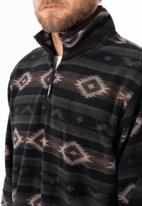 Man med en svart och brun mönstrad fleecepullover med halv dragkedja och dragkedja med "Hurley"-logotyp.