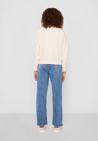 Ljusrosa bomberjacka med ribbade ärmslut och nederkant, kombinerad med löst sittande blå jeans och vita sneakers med Nike-logga på hälen.