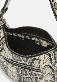 Czarna i biała torebka w z wzorem węża, o błyszczącej fakturze, z zamykanymi kieszeniami i miękką podszewką wewnętrzną.