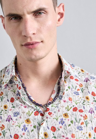 Floral short-sleeved shirt featuring a white background with colorful wildflower prints in red, yellow, blue, and purple. Collared design.