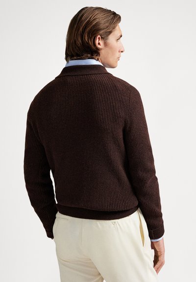 Brun teksturert cardigan med ribbet mønster og sjalkrage, båret over en lyseblå skjortekrage, med en figurnær passform.