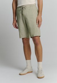 Lichtgroene, gestructureerde shorts met een elastische tailleband en trekkoord, met een ontspannen pasvorm en een knielange snit. Gecombineerd met crèmekleurige schoenen en sokken.