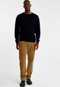 Marineblå sweater med rund hals, parret med lysebrune fløjlbukser. Sorte sko med strukturerede detaljer. Simpelt design og pasform.