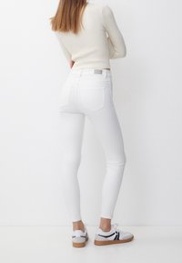 Vita smala jeans med hög midja, försedda med två bakfickor och en slät yta. Matchas med vita sneakers med svarta accenter.