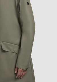 Olive green waterproof coat with a smooth texture, featuring a side pocket and black button accents on the sleeve and pocket flap.
