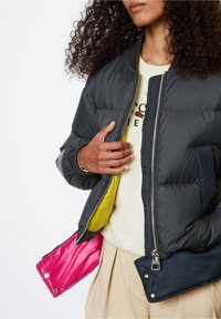 Black puffer jacket with zip closure, ribbed cuffs, and interior lined in vibrant yellow and pink. Features a side pocket and smooth texture.