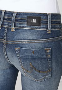 Jeans de mezclilla azul con un diseño ajustado, que cuentan con una etiqueta de marca LTB negra, costuras en contraste y un distintivo detalle en el bolsillo trasero.