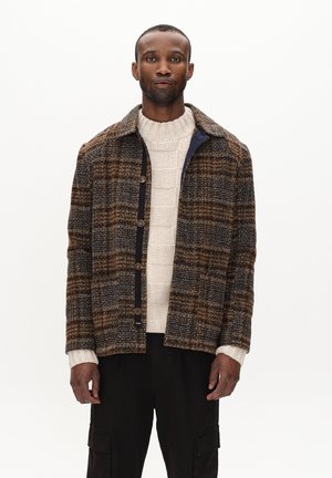 Brun og marineblåternet jakke med krave og knaplukning, båret over en cremefarvet kabelstrikket sweater med lange ærmer og lige snit.