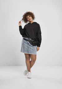 Sudadera con capucha negra, falda de mezclilla con dobladillo deshilachado y zapatillas blancas; la modelo lleva una riñonera negra; cabello rizado.