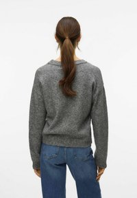 Pull gris à coupe décontractée, encolure large et ourlet côtelé. Porté avec un jean taille haute bleu, mettant en avant un style décontracté.