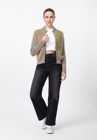 Πλεκτό μπουφάν σε ελιά πράσινο με υφή τριχωτή μπροστά και ριμπ μανίκια, σε συνδυασμό με ψηλόμεσα μαύρα τζιν και λευκά αθλητικά παπούτσια.