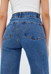 Hoge taille blauwe spijkerbroek met een vervaagde wassingen, voorzien van twee achterzakken en contrasterende stiksel. De stof is gestructureerd en stevig.