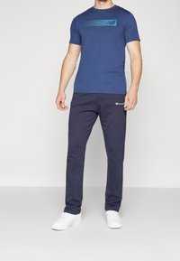 Marinblå t-shirt med en teal grafisk rand och matchande marinblå sweatpants. Vita sneakers fulländar den atletiska outfiten. Mjukt, avslappnat tyg.