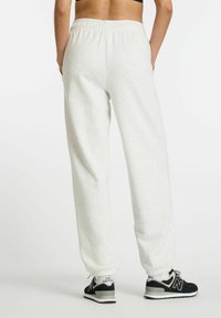 Helle graue, legere Sweatpants mit einem elastischen Bund und schmal zulaufenden Bündchen, kombiniert mit schwarzen New Balance Sportschuhen.