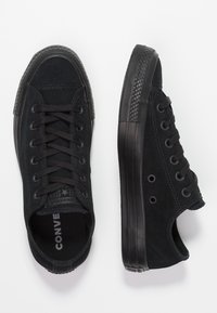 Černé nubukové nízké tenisky mají kulaté šňůrky, gumovou podrážku a texturovanou špičku. Branding je viditelný na stélce a po straně.