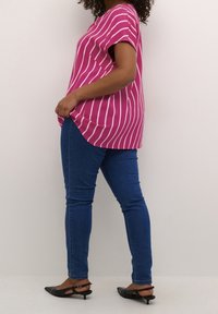 Blouse rayée rose à manches courtes, ourlet arrondi, associée à un jean skinny bleu et des ballerines noires à bout pointu. Texture de tissu lisse.