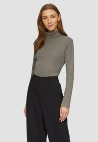 Langsleeve coltrui in olijfgroen katoen, met een getailleerd ontwerp en zachte textuur, gecombineerd met hoge taille zwarte broek.
