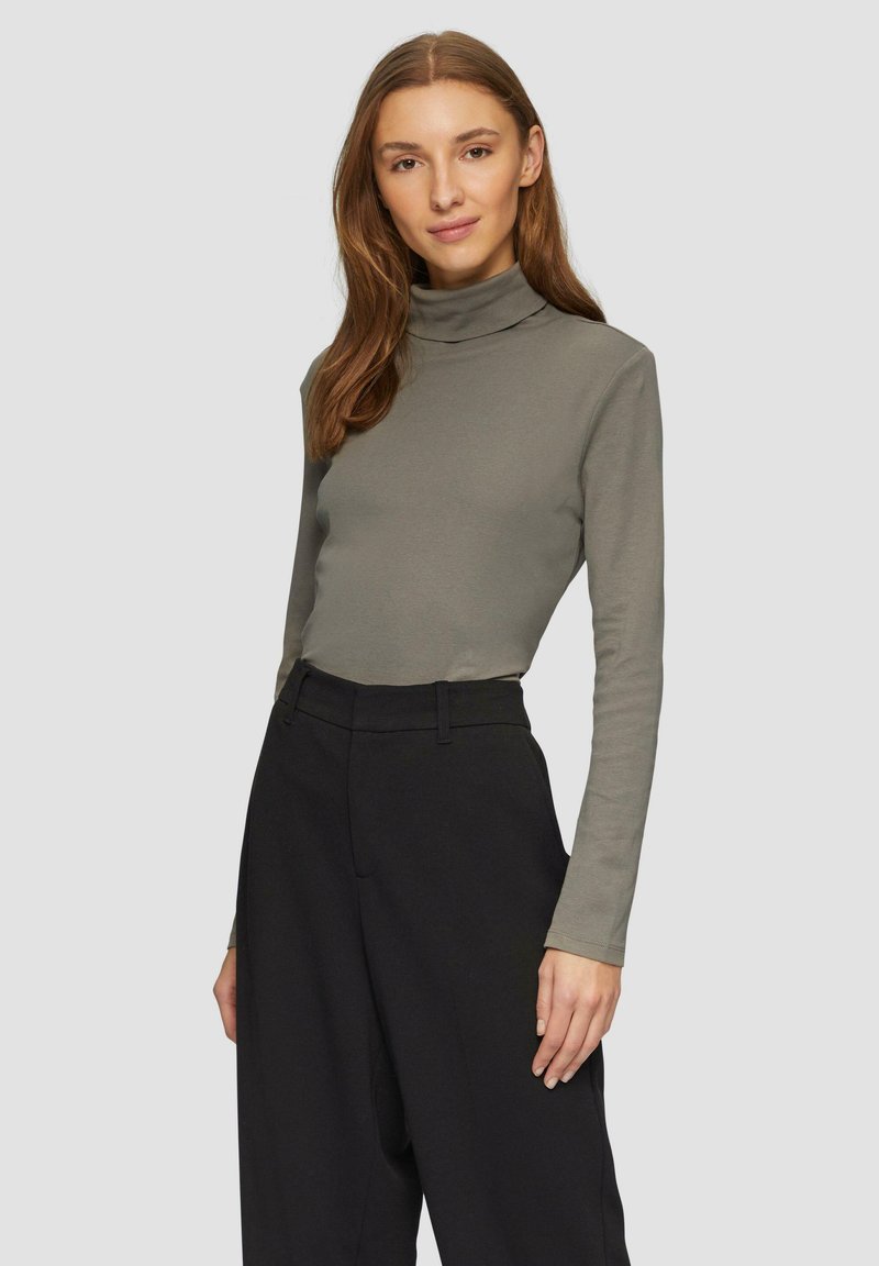 Langärmeliger Rollkragenpullover aus olivgrünem Baumwollmaterial, mit einem figurbetonten Design und weichem Griff, kombiniert mit hochgeschnittenen schwarzen Hosen.