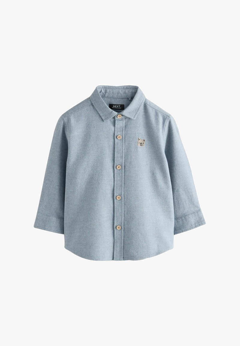 Gaiši zils garām piedurknēm krekls, izgatavots no mīksta auduma, ar pogu aizdari priekšā un mazu lāča izšuvumu uz krūts. Apaļa apkakle, klasiskā piegriezuma.