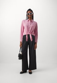 Pink striped button-up shirt tied at the waist, paired with dark wide-leg trousers. Black flats and a small black handbag complete the look.