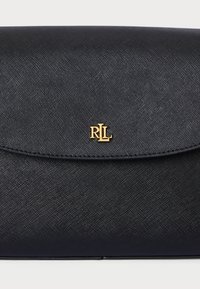 Bolsa preta feita de um material sintético texturizado. Apresenta um fecho em aba arredondada e um detalhe em logo dourado no centro.