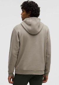 Kapuzensweatshirt in Taupe, mit weicher Textur und gerippten Bündchen. Das Design ist lässig geschnitten, mit einer sichtbaren Naht entlang des Rückens.