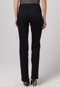 Jean noir à coupe slim, avec poches arrière et ceinture standard. Porté avec des talons hauts. Texture lisse et sans motifs visibles.