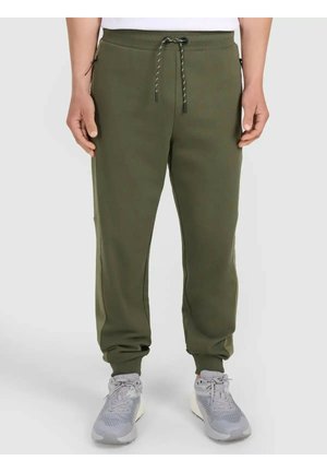 Proste spodnie dresowe w oliwkowym zielonym kolorze z regulacją w talii i zapinanymi na zamek kieszeniami bocznymi, noszone z jasnoszarymi sneakersami.