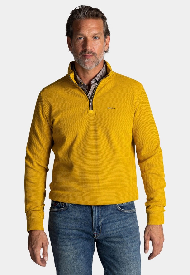 Geel pullover trui met een half-rits kraag, geribbelde textuur en logodetail, gecombineerd met blauwe jeans.
