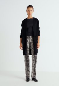 Svart lång cardigan med öppen front, buren över en figursydd topp, i kombination med mönstrade grå byxor med zebramönster. Svarta klackskor.
