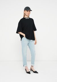 Must have suurusega must t-särk valge logoga, heledad sinised rullitud teksad, mustad slingback kontsad kaunistustega ja tumehall pesapallikepiga müts.