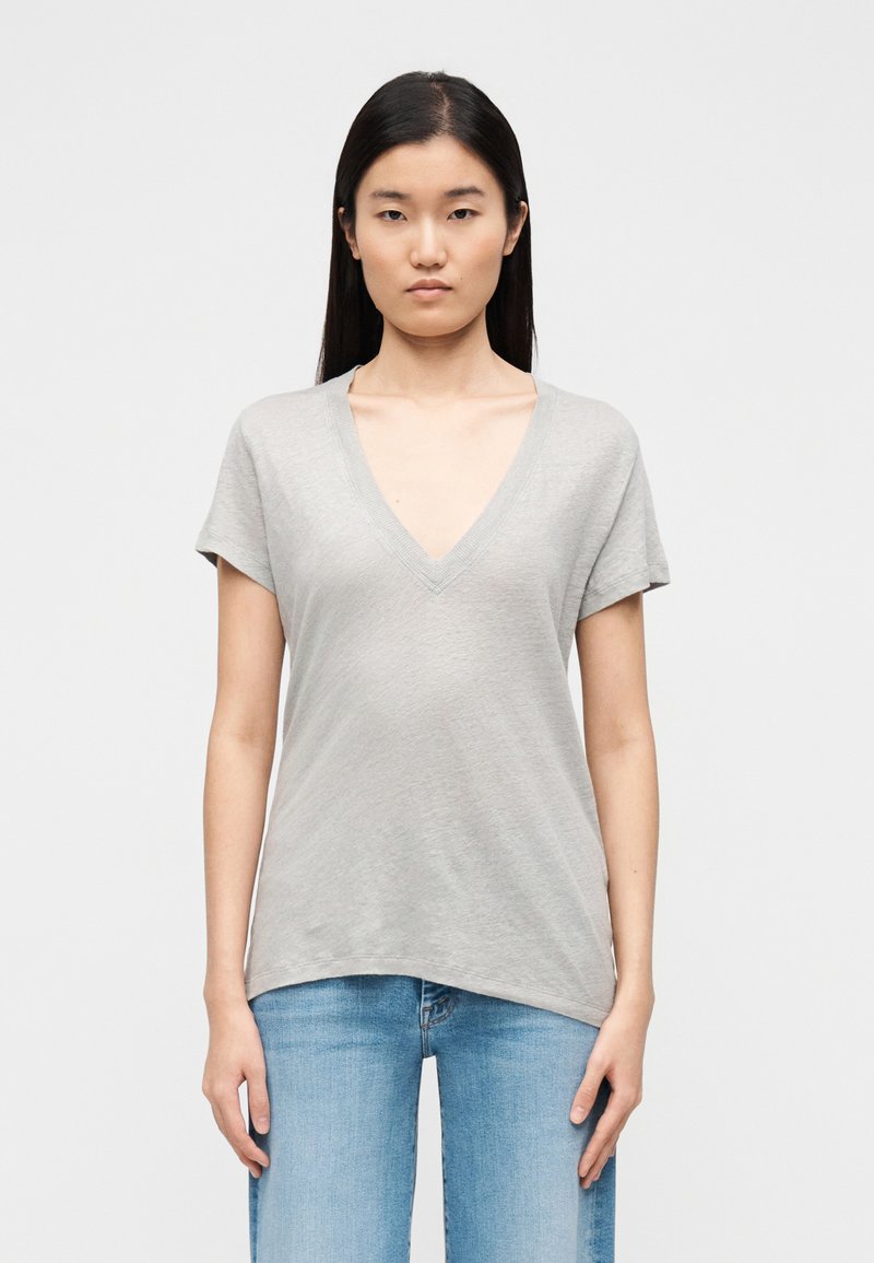 T-shirt cinzenta com decote em V, feita de tecido macio, com mangas curtas e corte descontraído, combinada com jeans azul claro.